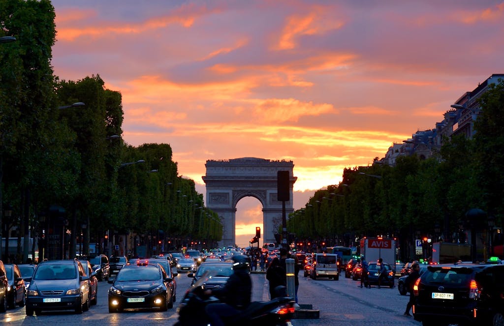 Vivid sunset sky over Arc de Triomphe, capturing Parisian traffic and architecture.